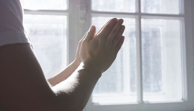 Praying hands pressed together at backlit window morning light