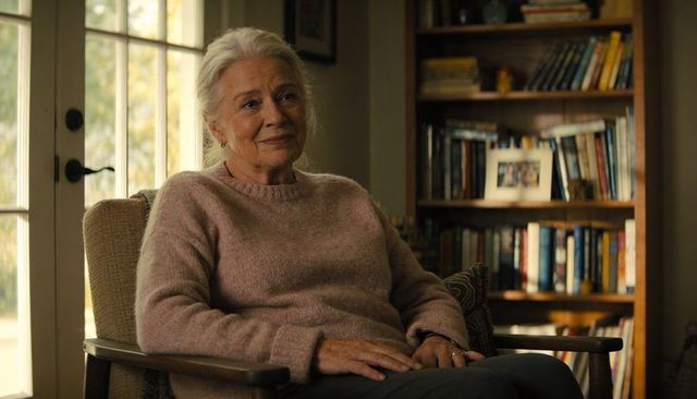 Senior woman sitting in armchair wearing pink sweater and pants, serene sunlit portrait