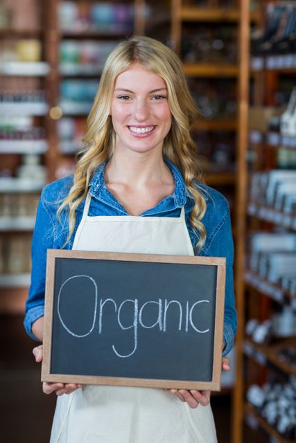 Portrait of smiling female staff holding a organic sign board in supermarket