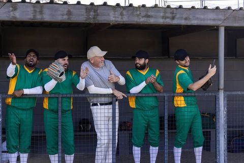 Baseball team cheering in dugout with coach directing lineup at ballpark in green uniforms