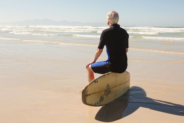 Rear view of senior man sitting on surfboard against clear sky