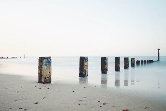 Wooden pillars stretching out into the calm sea at dawn, reflecting serene and tranquil atmosphere. Ideal for themes of nature, travel, morning calmness or coastal beauty. Perfect for use in websites, blogs, and promotional material that highlight peaceful and scenic beach locations.