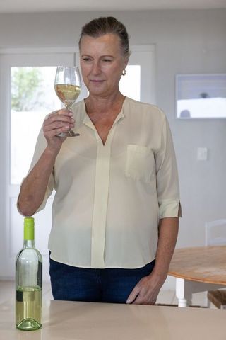Senior woman examining wine glass in modern kitchen