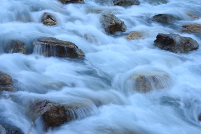 Dynamic depiction of a rushing river stream with water creating a smooth, blurred effect against rocks. Image is ideal for promoting adventure travel, outdoor activities, nature reserves, and serenity themes. Perfect for websites, brochures, and advertisements related to nature, environment, and relaxation.