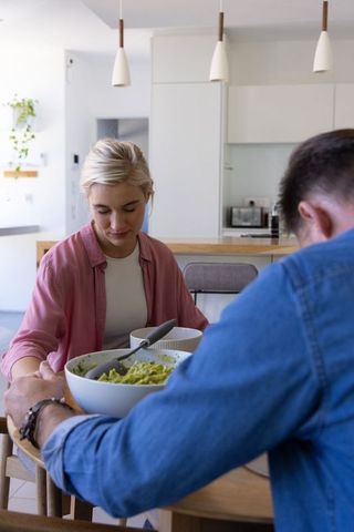 Couple sharing healthy salad at modern kitchen table, casual home meal and connection