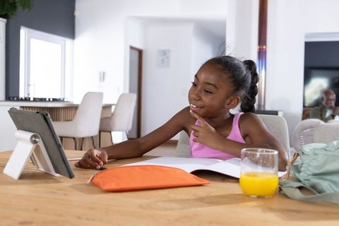 African american girl learning with tablet and workbook at kitchen table in bright home