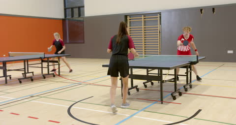 Teenagers energetically play table tennis in a school gym, highlighting their focus and competitive spirit. This video is ideal for content related to teenage sports, physical education classes, team activities, or school gym scenarios, demonstrating team interaction, athletic skills, and youth engagement in organized games.