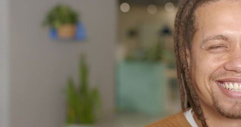 Smiling man with dreadlocks and goatee in modern reception area, turquoise bokeh, left copy space