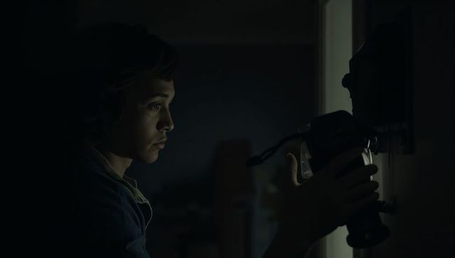Young woman adjusting wall-mounted security camera in dim corridor, moody surveillance