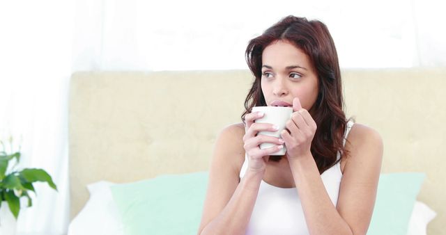 Smiling woman holding mug on bed at home
