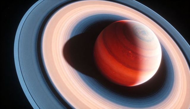 Scarlet ringed gas giant casting deep shadow across multicolored planetary rings