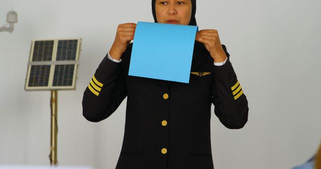 Professional female pilot in uniform conducts training session, holding a blue paper, emphasizing important points. Ideal for use in educational content, aviation training materials, promotional materials for flight schools, and articles highlighting gender equality in aviation.