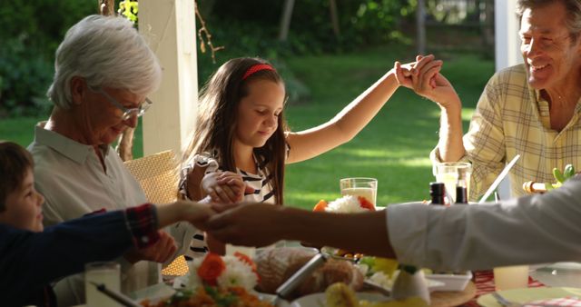 Happy caucasian family holding hands and praying before dinner in sunny garden. Domestic life, family, food and lifestyle, unaltered.