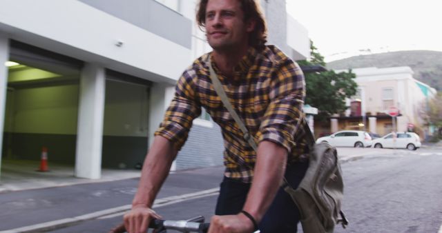 Young man riding bicycle through urban street with messenger bag - Download Free Stock Images Pikwizard.com