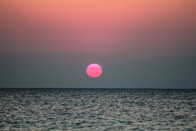 Vibrant sunset over calm ocean on horizon with soft pink and blue colors. Perfect for backgrounds, travel blogs, inspirational quotes, and nature-related content. Ideal for conveying relaxation and tranquility.