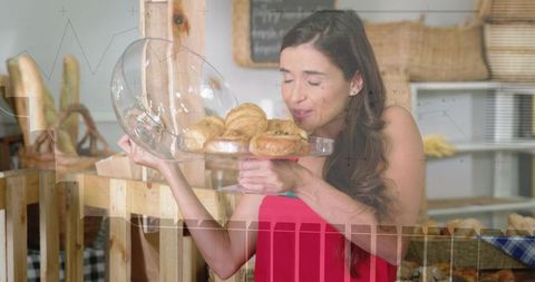 Woman smelling fresh pastries under glass cloche in rustic bakery, cozy market moment