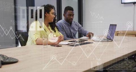 Business team reviewing data at conference table with laptop and analytics charts overlay