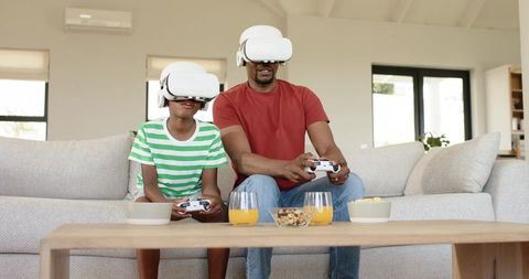 African American father and son using VR headsets playing together on couch