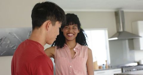 Woman resting arm on partner's shoulder while couple laugh in bright modern kitchen