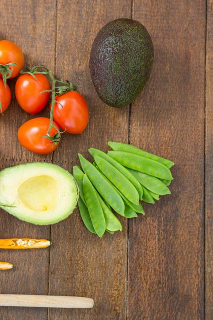 Fresh organic vegetables including avocado, tomatoes, and snap peas laid out on a rustic wooden board. Ideal for use in culinary blogs, recipe websites, healthy eating promotional materials, and farm-to-table dining advertisements.