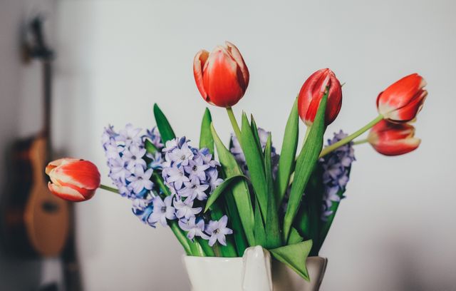 Vibrant red tulips and light purple hyacinths arranged in white vase bring touch of nature and freshness to home interior. Perfect for use in lifestyle blogs, interior design websites, and spring seasonal promotions.