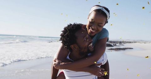 Couple sharing piggyback joy on sunny beach with gold star confetti and rolling waves