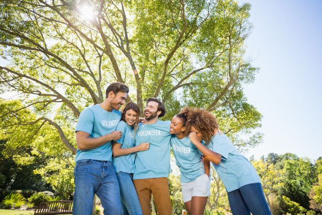 Group of diverse volunteers laughing and bonding in a park on a sunny day. Ideal for use in campaigns promoting community service, teamwork, charity events, and outdoor activities. Perfect for illustrating concepts of friendship, unity, and positive social impact.