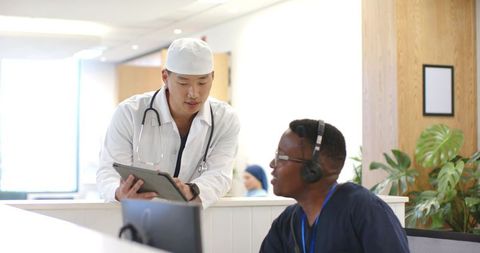 Physician consulting front desk staff with tablet in modern clinic reception, teamwork