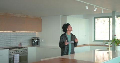 Man inspecting modern kitchen while holding tablet at minimalist island, smart home interior