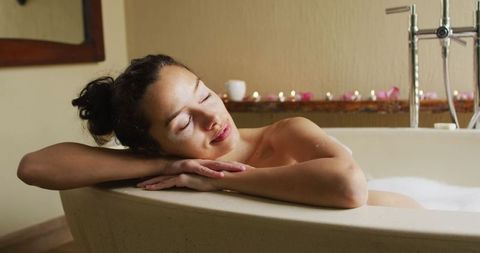 Peaceful woman with vitiligo relaxing in bubble bath with candles