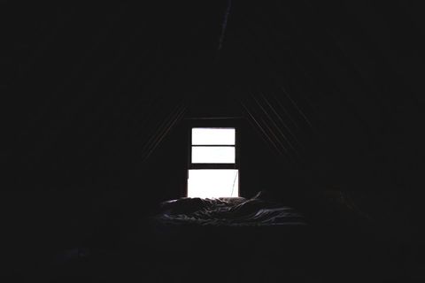 Dimly lit attic with small window and bedding