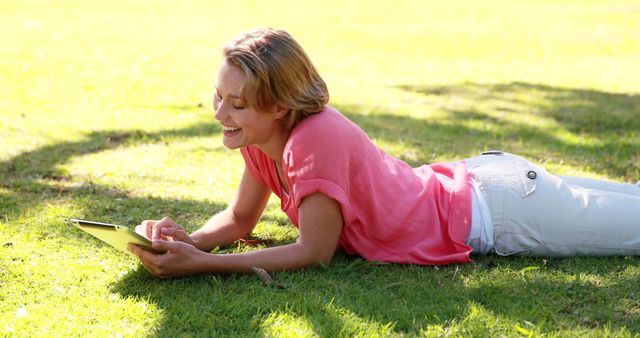 Smiling Woman Lying on Grass Using Tablet in Sunny Park - Download Free Stock Images Pikwizard.com