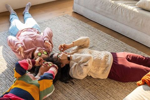 Diverse friends enjoying cozy at-home spa night with cucumber eye patches and knit sweaters