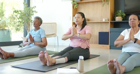 African american senior women practicing seated yoga together in bright sunlit studio
