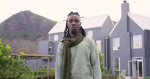 African american man standing in modern front yard in sage sweater and olive scarf