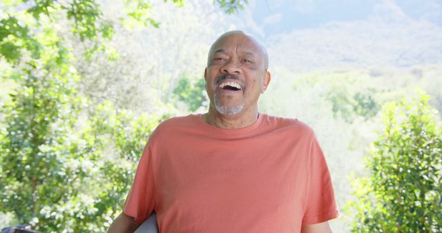 Portrait of happy senior bald african american man laughing in sunny nature, slow motion. Summer, retirement, wellbeing and healthy senior lifestyle, unaltered.