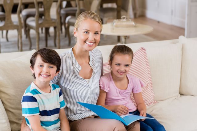 Portrait of smiling mother and kids sitting on sofa with book in living room