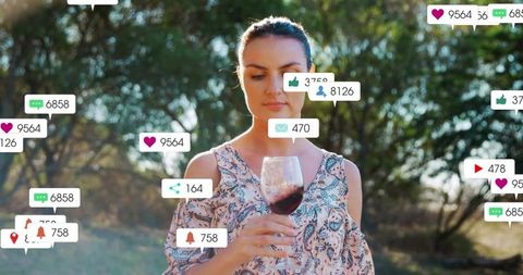 Woman gazing at wine glass as social media likes comments shares float during golden hour