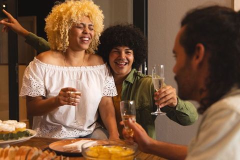 Laughing friends clinking champagne flutes and toasting at cozy home dinner party