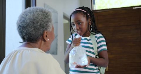 African american granddaughter presenting goldfish in bag to smiling senior woman at door