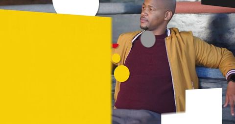 Urban man leaning on bench wearing mustard bomber jacket with bold yellow graphic overlay