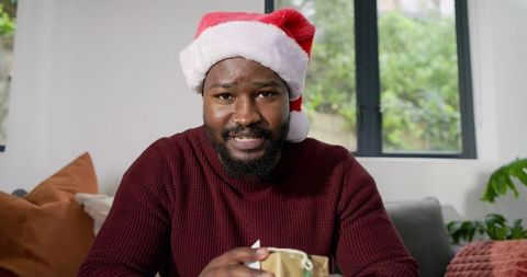 African American Man Wearing Santa Hat Holding Wrapped Gift on Cozy Living Room Couch