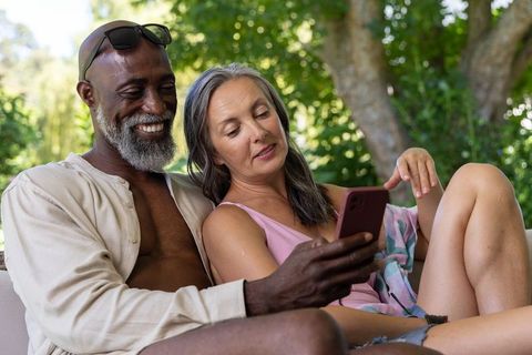 Senior couple relaxing on outdoor sofa sharing smartphone and enjoying sunny garden moment