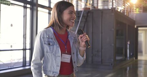 Indian woman presenting with microphone and blue lanyard in modern conference space