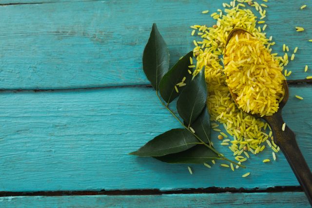This image shows raw organic yellow rice and fresh curry leaves on a rustic wooden table. Ideal for use in food blogs, cooking websites, recipe books, and health-related articles. Perfect for illustrating natural and organic ingredients in culinary contexts.