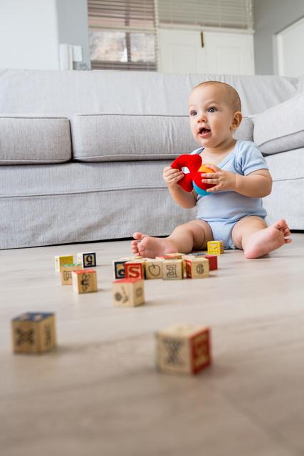 Baby boy sitting on floor playing with colorful toys and blocks in a living room. Ideal for use in parenting blogs, early childhood education materials, family lifestyle articles, and advertisements for baby products.