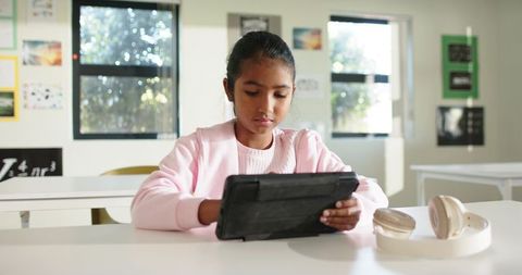 Asian teen girl studying on tablet in bright classroom, focused remote learning