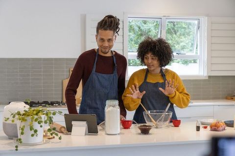 African american couple baking together on kitchen island using tablet and denim aprons