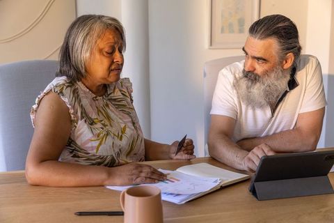 Senior couple reviewing finances at home, woman holding card while discussing budget and bills