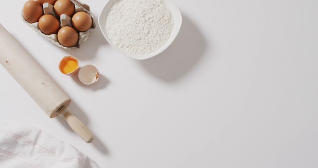 A flat lay of baking essentials including a rolling pin, a carton of eggs, a bowl of flour, and a cracked egg on a white background. Ideal for use in culinary blogs, cooking websites, recipe illustrations, and kitchenware advertisements. The minimalist style and white background ensure the focus remains on the baking items, making it perfect for tutorial visuals and ingredient listings.